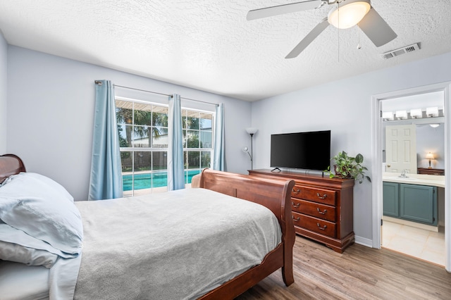 bedroom featuring ceiling fan, a textured ceiling, ensuite bath, and light hardwood / wood-style floors