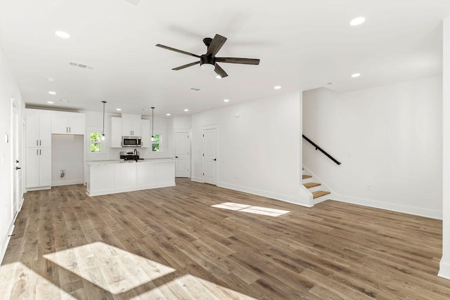 unfurnished living room with recessed lighting, visible vents, light wood-style flooring, baseboards, and stairs