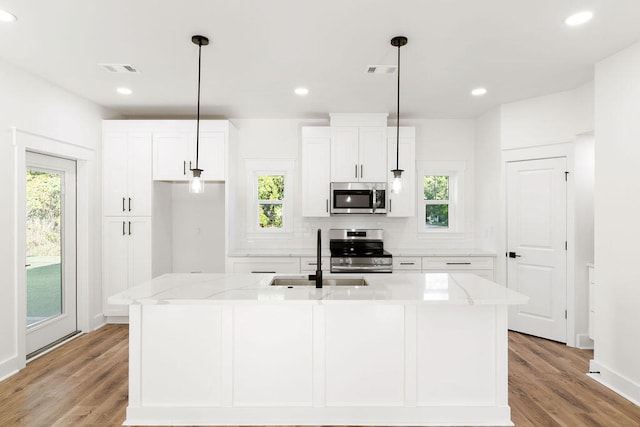 kitchen with white cabinets, an island with sink, appliances with stainless steel finishes, light stone countertops, and a sink