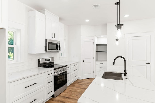 kitchen with light stone counters, decorative light fixtures, stainless steel appliances, white cabinetry, and a sink