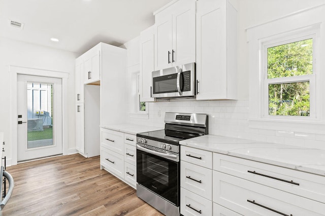 kitchen with light stone counters, stainless steel appliances, visible vents, white cabinetry, and decorative backsplash