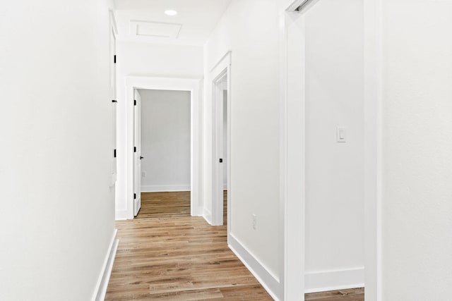 corridor with light wood-style flooring, baseboards, and attic access