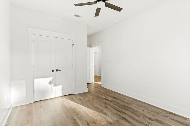 unfurnished bedroom with a closet, visible vents, a ceiling fan, wood finished floors, and baseboards