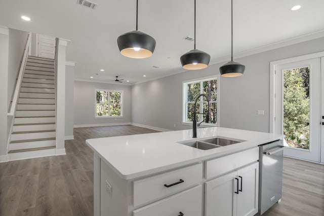 kitchen featuring a center island with sink, light countertops, hanging light fixtures, stainless steel dishwasher, and a sink