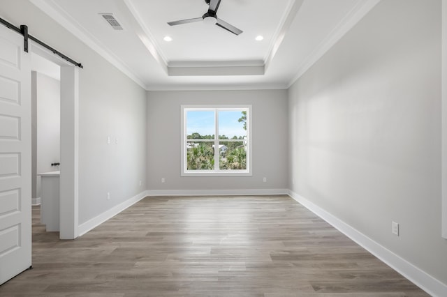 empty room with a barn door, visible vents, a ceiling fan, a tray ceiling, and crown molding