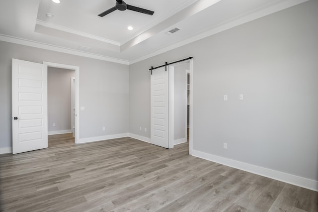 unfurnished bedroom with a tray ceiling, crown molding, light wood finished floors, visible vents, and a barn door