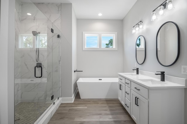 full bathroom featuring a marble finish shower, double vanity, a soaking tub, a sink, and wood finished floors