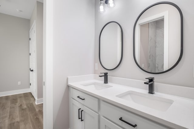 bathroom featuring wood finished floors, a sink, baseboards, and double vanity