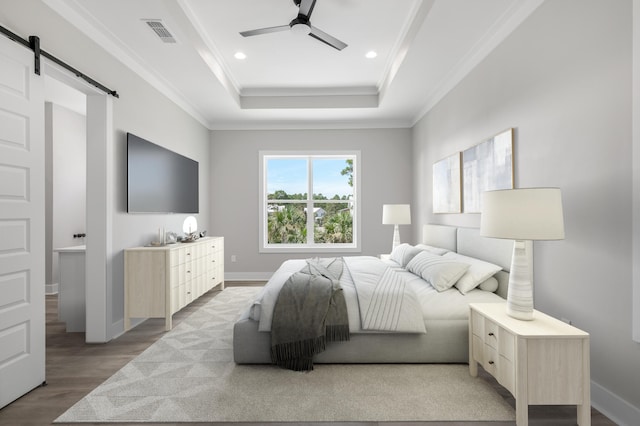 bedroom featuring a barn door, visible vents, a raised ceiling, ornamental molding, and wood finished floors