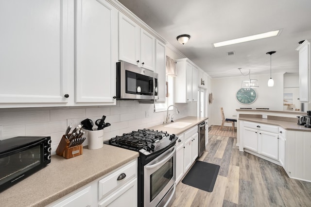 kitchen with appliances with stainless steel finishes, sink, light wood-type flooring, decorative light fixtures, and white cabinets