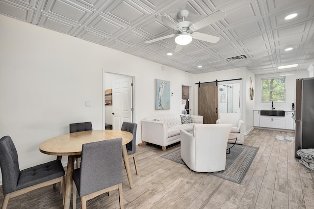 dining area with ceiling fan, a barn door, sink, and light hardwood / wood-style flooring