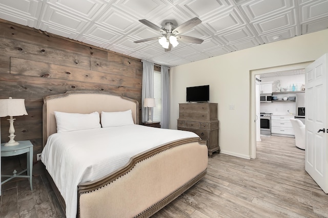 bedroom with ceiling fan, wood walls, and light hardwood / wood-style floors