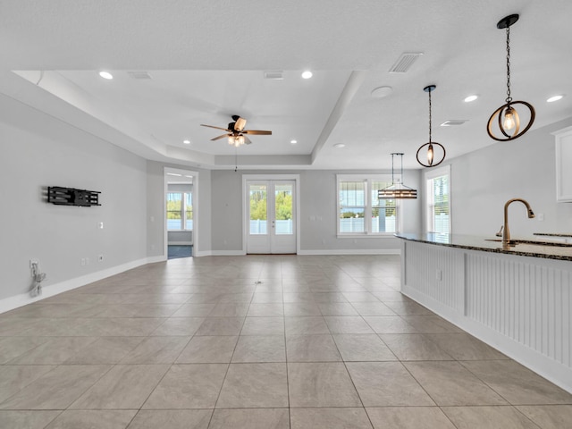 unfurnished living room with sink, light tile patterned flooring, french doors, a raised ceiling, and ceiling fan