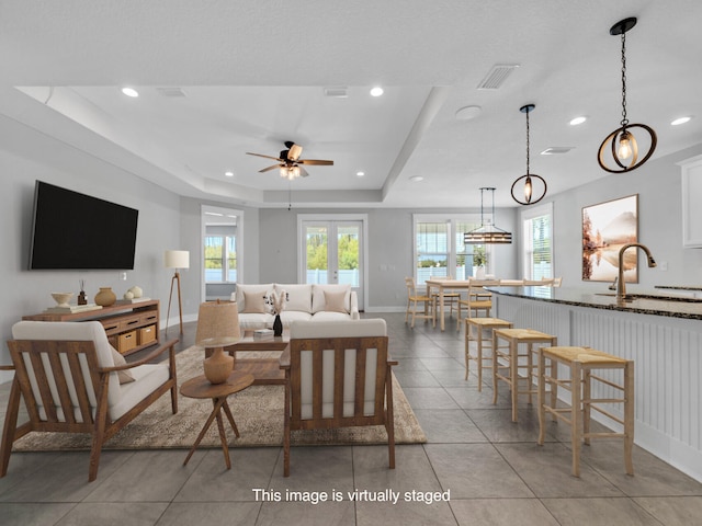 living room with ceiling fan, a tray ceiling, light tile patterned flooring, french doors, and sink