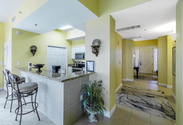 kitchen featuring appliances with stainless steel finishes, white cabinetry, light tile patterned floors, and dark stone counters