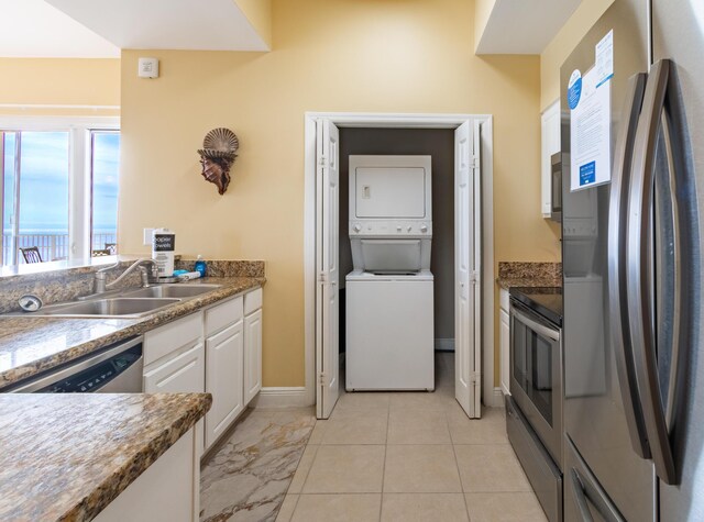 kitchen with light tile patterned flooring, stacked washer and clothes dryer, sink, stainless steel appliances, and white cabinets