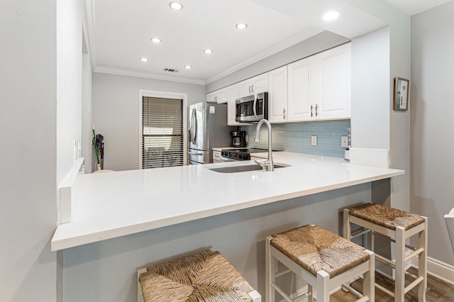 kitchen featuring kitchen peninsula, appliances with stainless steel finishes, a kitchen breakfast bar, sink, and white cabinetry