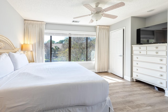 bedroom with a textured ceiling, light hardwood / wood-style flooring, and ceiling fan