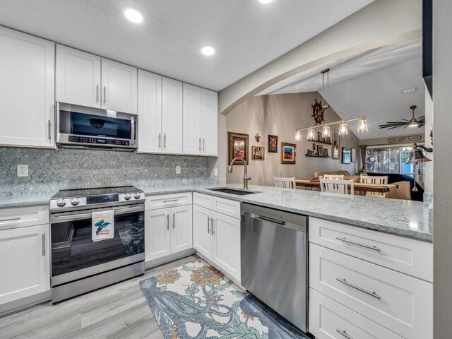 kitchen with white cabinets, appliances with stainless steel finishes, light stone counters, light hardwood / wood-style floors, and sink