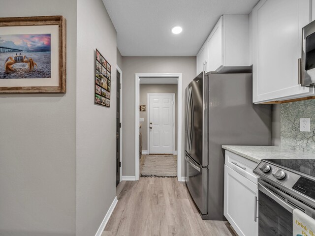 kitchen featuring stainless steel appliances, light hardwood / wood-style floors, white cabinets, and tasteful backsplash