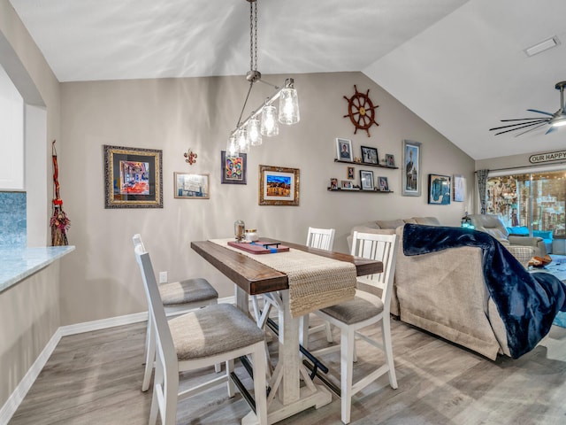 dining space with lofted ceiling, ceiling fan with notable chandelier, and hardwood / wood-style flooring