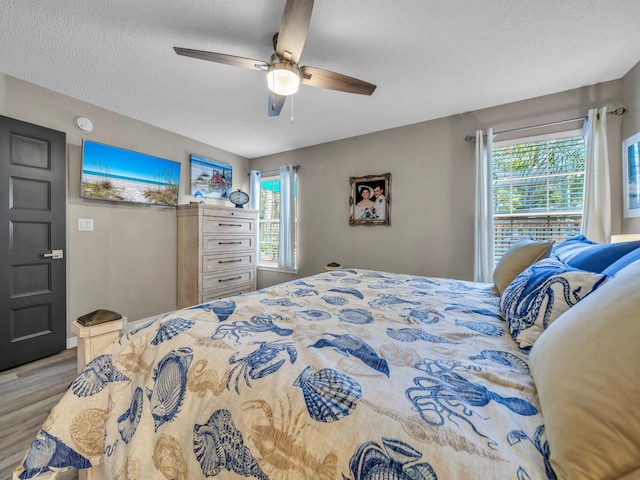 bedroom with ceiling fan, light wood-type flooring, a textured ceiling, and multiple windows