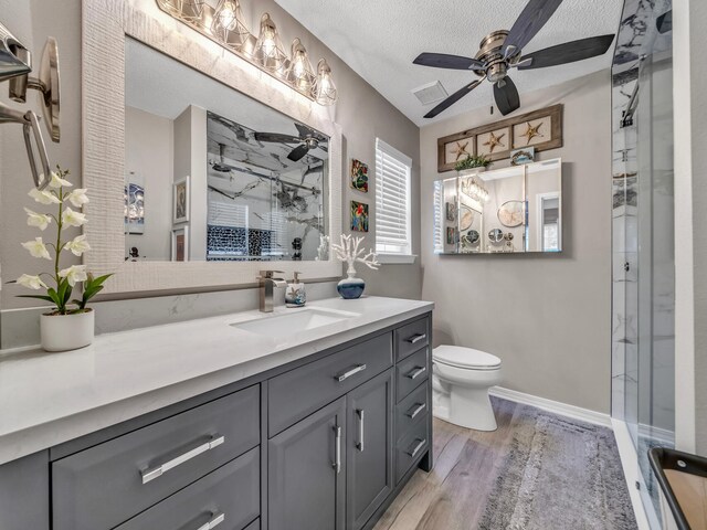 bathroom with ceiling fan, toilet, vanity, hardwood / wood-style flooring, and a textured ceiling