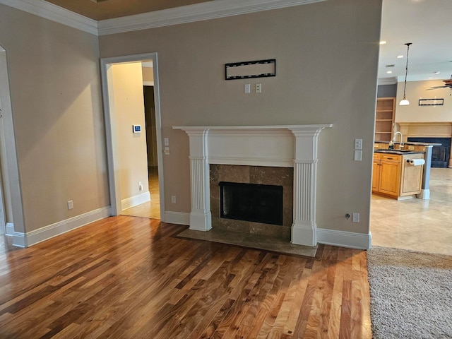 unfurnished living room featuring sink, a tiled fireplace, hardwood / wood-style floors, ornamental molding, and ceiling fan