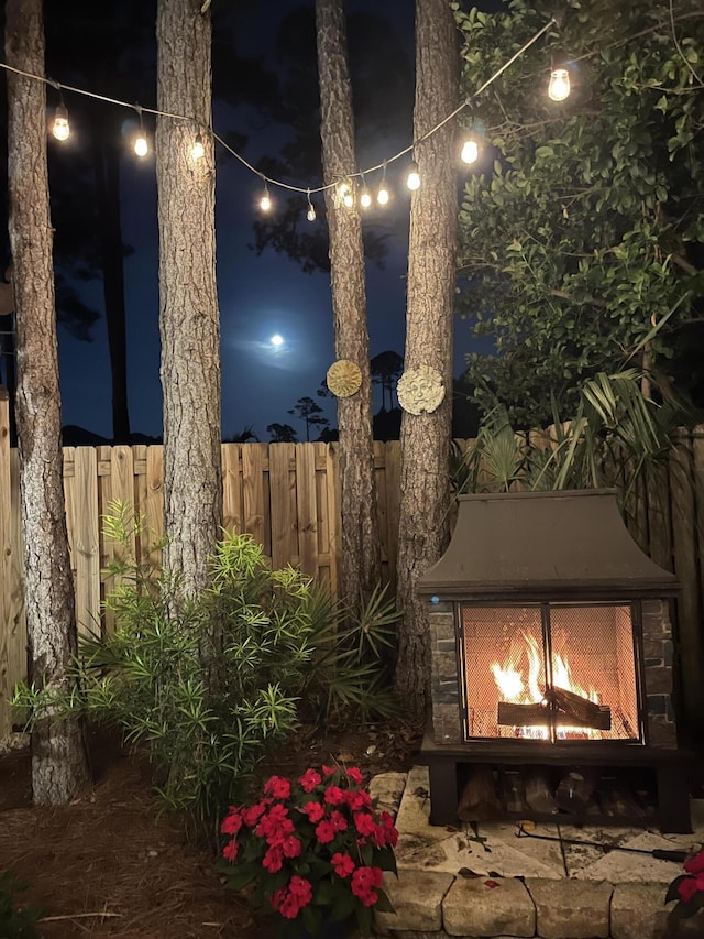 patio at twilight featuring a lit fireplace and fence