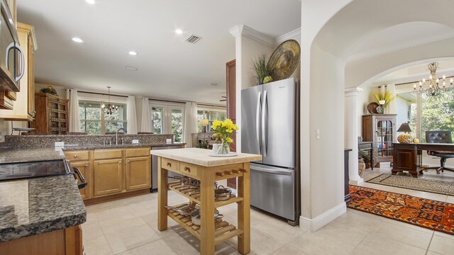 kitchen with light tile patterned flooring, stainless steel appliances, ornamental molding, and an inviting chandelier