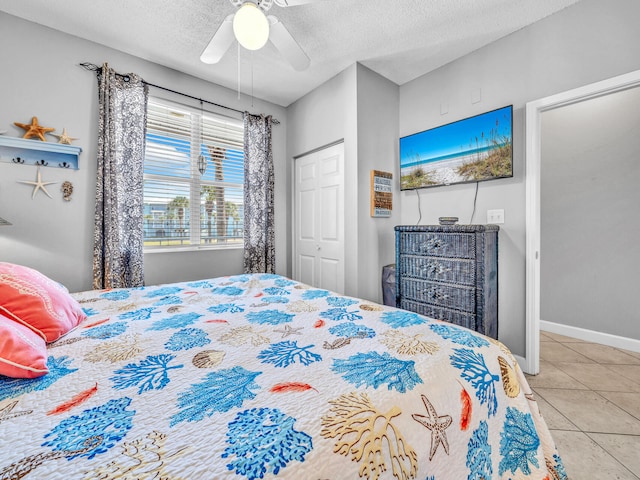 bedroom featuring light tile patterned floors, baseboards, a ceiling fan, a textured ceiling, and a closet