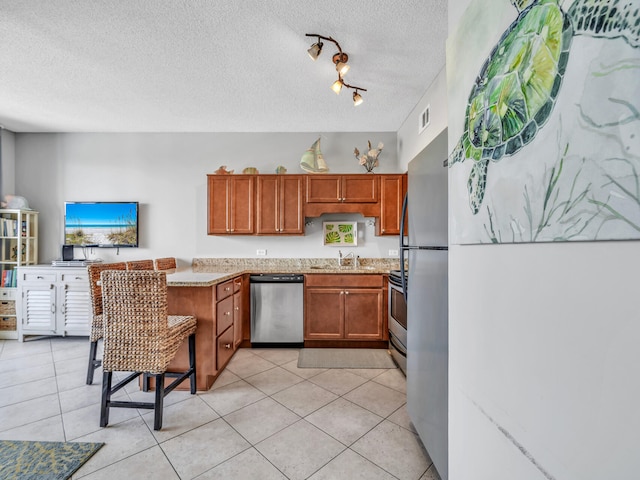 kitchen featuring light tile patterned floors, stainless steel appliances, brown cabinetry, a sink, and a textured ceiling