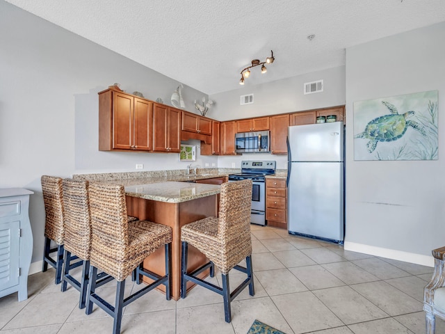 kitchen with a peninsula, a breakfast bar, visible vents, appliances with stainless steel finishes, and brown cabinets