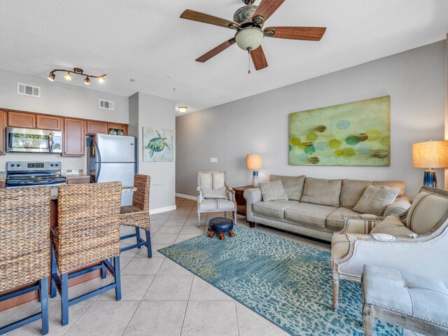 tiled living room with ceiling fan, track lighting, and a textured ceiling