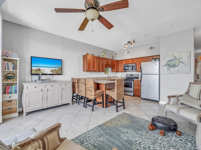 living area with a ceiling fan, visible vents, a textured ceiling, and light tile patterned flooring