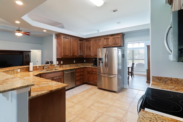 kitchen featuring appliances with stainless steel finishes, light stone counters, light hardwood / wood-style floors, ceiling fan, and kitchen peninsula