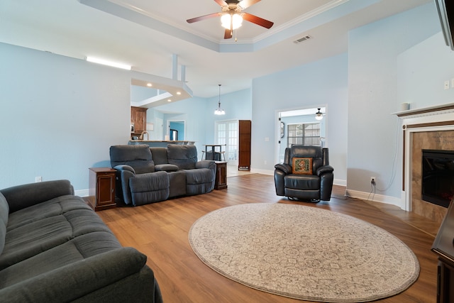 living room featuring ceiling fan, a fireplace, light wood-type flooring, and a high ceiling