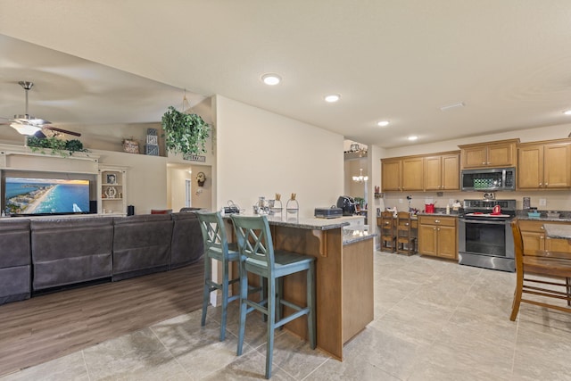 kitchen with a kitchen breakfast bar, light wood-type flooring, stone countertops, ceiling fan, and stainless steel appliances