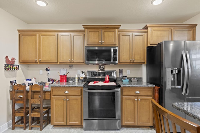 kitchen featuring dark stone countertops, a textured ceiling, appliances with stainless steel finishes, and light tile patterned floors