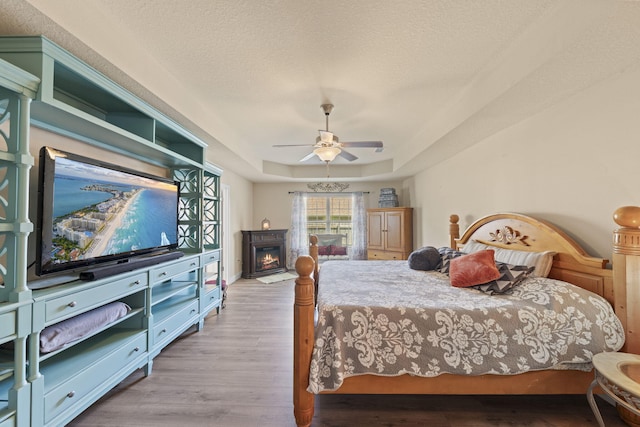 bedroom featuring ceiling fan, a raised ceiling, light hardwood / wood-style flooring, and a textured ceiling