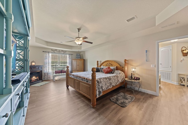 bedroom featuring ceiling fan, a textured ceiling, light hardwood / wood-style flooring, and a tray ceiling