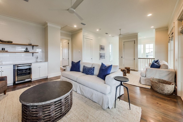 living room with ceiling fan, wet bar, hardwood / wood-style floors, ornamental molding, and wine cooler