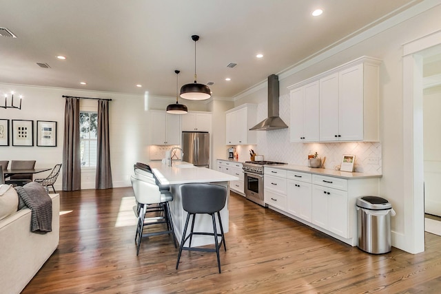 kitchen featuring white cabinets, stainless steel appliances, wall chimney exhaust hood, and decorative light fixtures