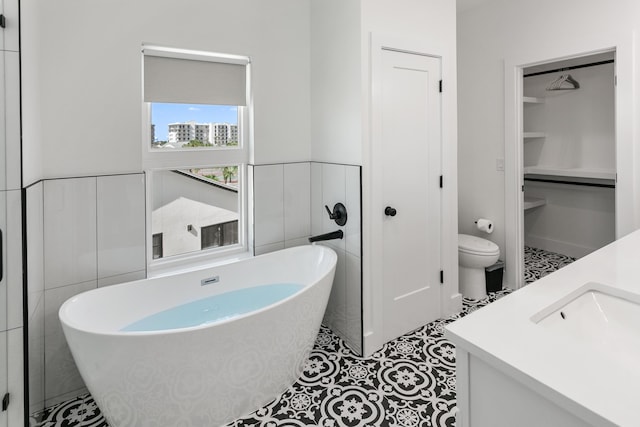 bathroom with tile walls, a bathtub, vanity, tile patterned floors, and toilet