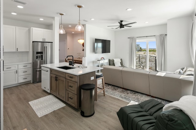 kitchen with high end fridge, sink, white cabinetry, white dishwasher, and an island with sink