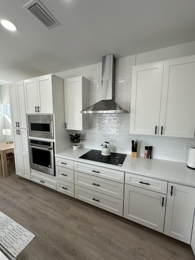 kitchen featuring white cabinetry, stainless steel appliances, decorative backsplash, and wall chimney range hood