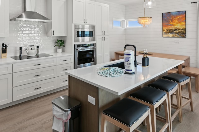 kitchen with hanging light fixtures, a breakfast bar, white cabinets, and wall chimney exhaust hood