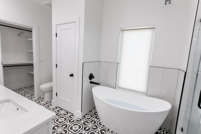 bathroom with a washtub, tile walls, vanity, tile patterned floors, and toilet