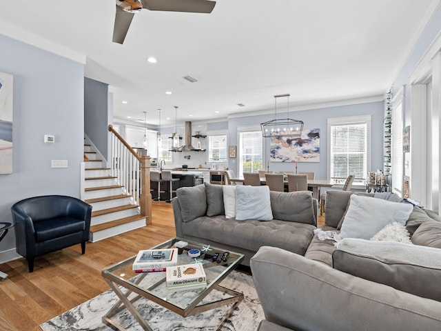 living room with ceiling fan with notable chandelier, crown molding, and light hardwood / wood-style flooring