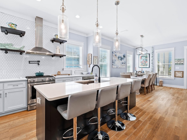 kitchen with decorative light fixtures, gas range, wall chimney exhaust hood, and an island with sink